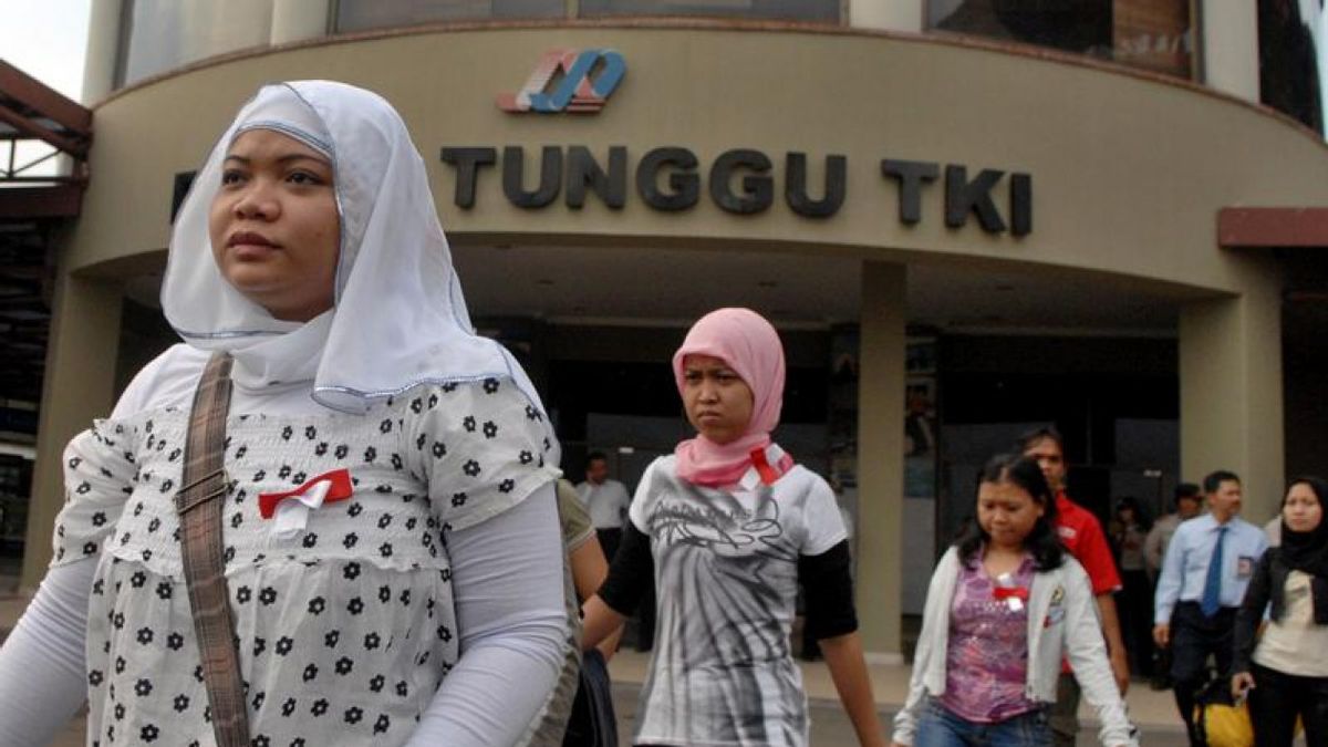  Indonesian migrant workers wearing headscarves walk in front of a building with a sign that reads "Tunggu TKI" which means "Waiting for Indonesian Migrant Workers".