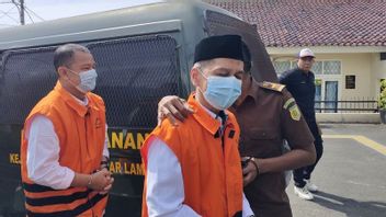 手錠をかけられたオレンジ色のベストを着て、カロマニと2人の被告がユニラ首相の贈収賄事件の起訴状読み上げに関する審理に出席